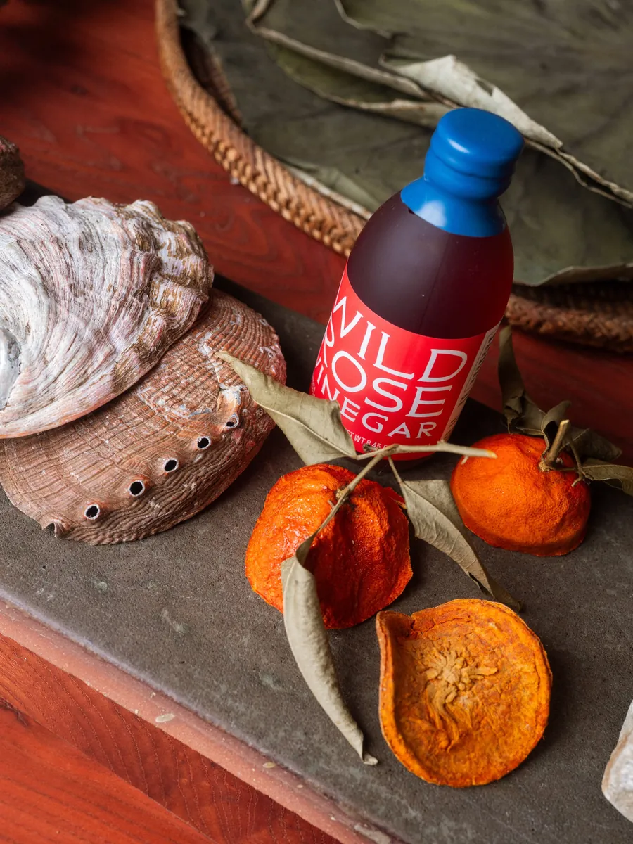 Una botella de Wild Rose Vinegar de Noma Projects con mandarinas secas y una concha